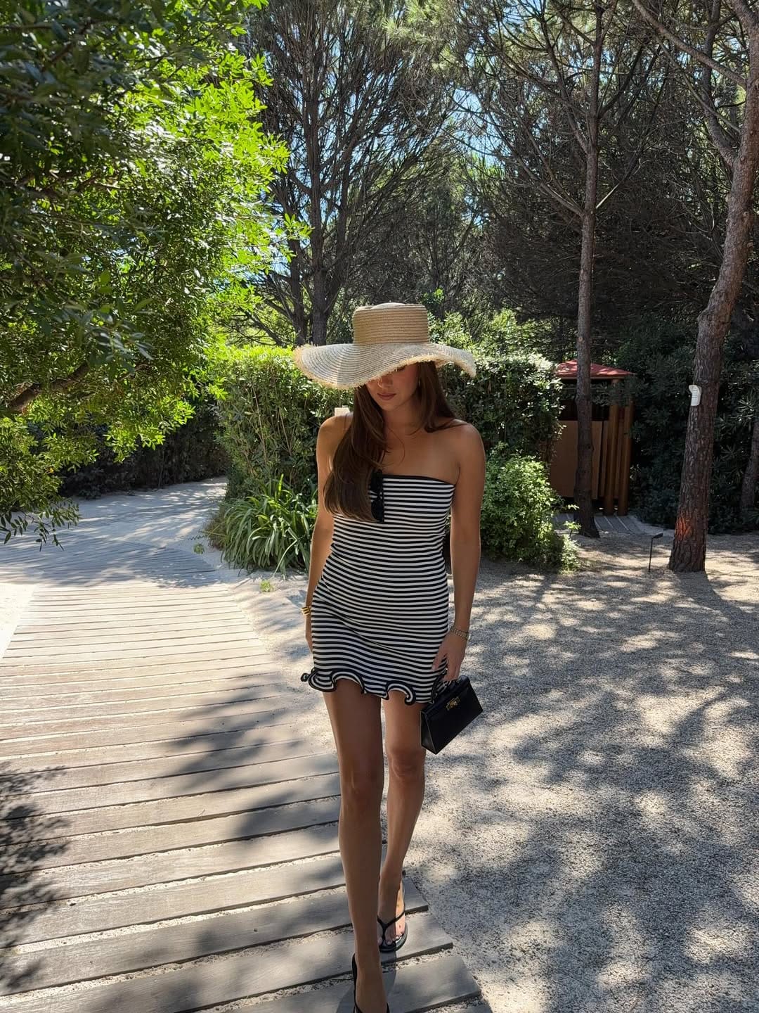 A black and white striped strapless mini dress with a ruffle hem, styled with a wide-brim straw hat for a playful vibe.
