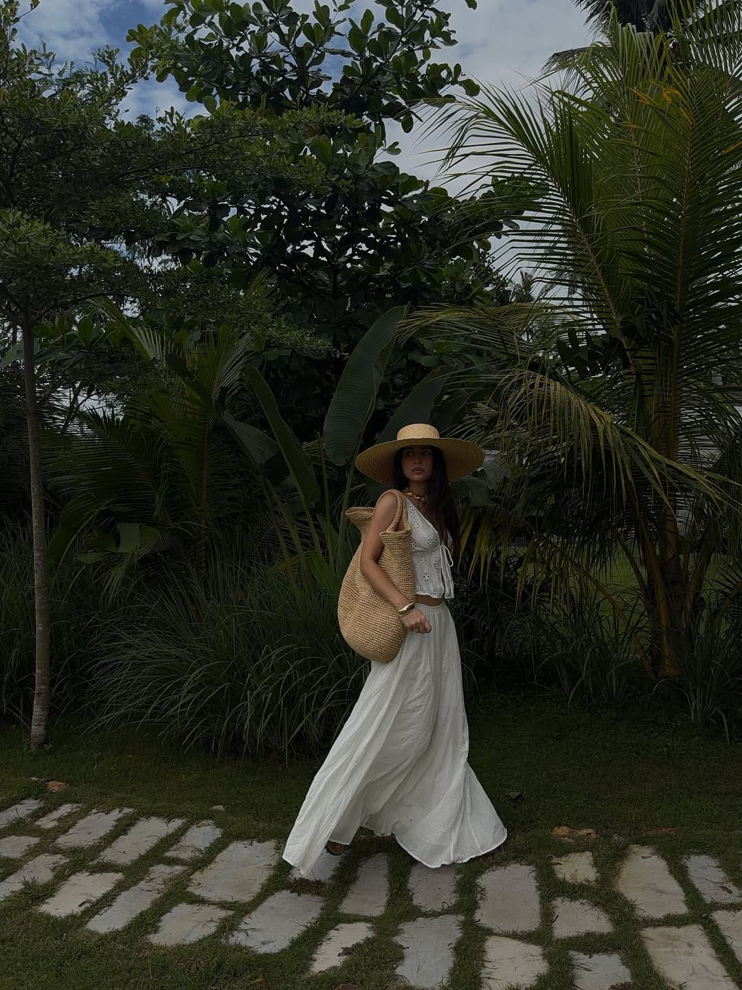 A white broderie anglaise crop top paired with a flowing white linen maxi skirt and a wide-brim hat for a classic resort look.
