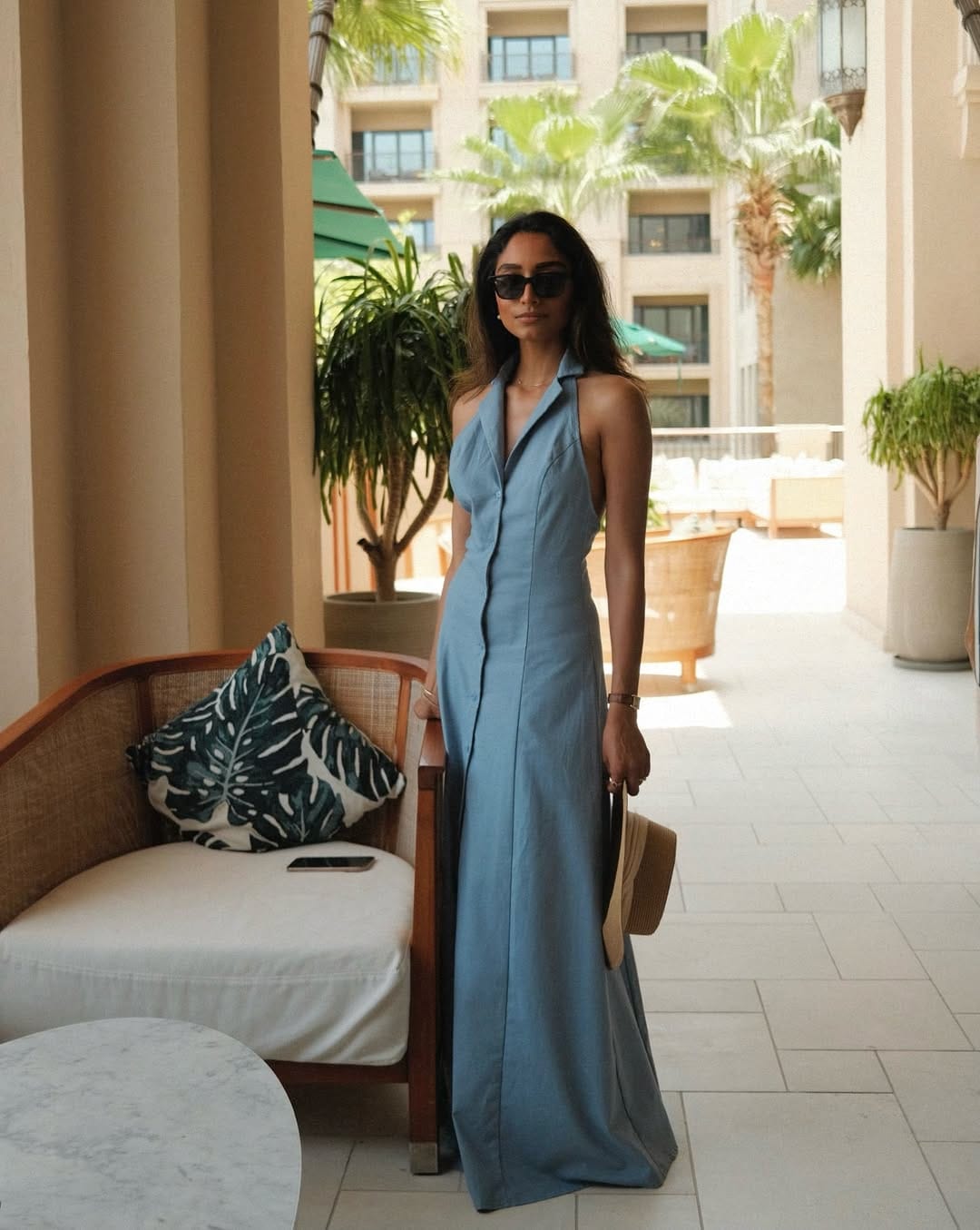 A blue linen halter neck maxi dress styled with a raffia tote, ideal for a relaxed seaside outfit.