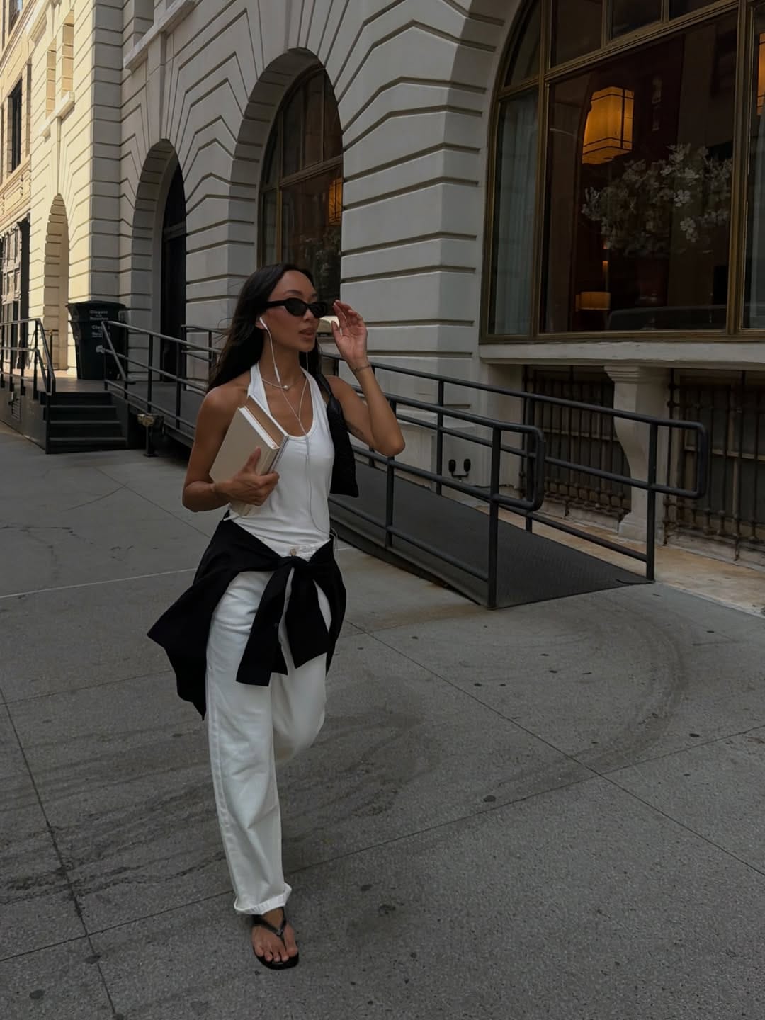 Woman in white halter tank and white jeans with black overshirt tied at the waist on a downtown Manhattan street, casual NYC summer outfit