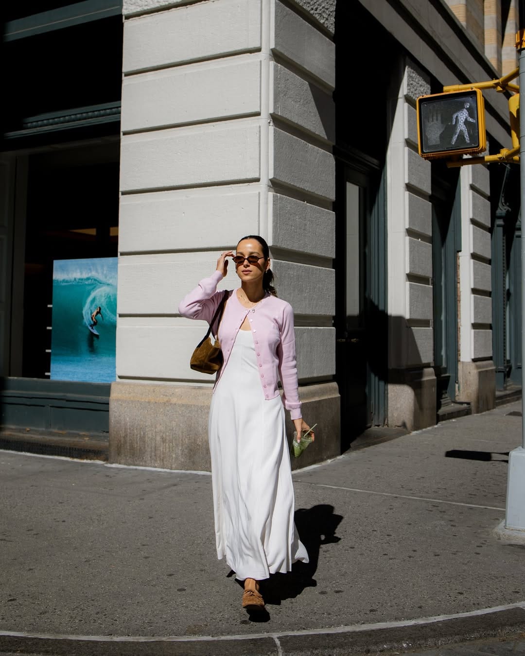 Woman in lilac fine-knit cardigan layered over white satin slip maxi dress with camel suede loafers on a sunny New York City street corner
