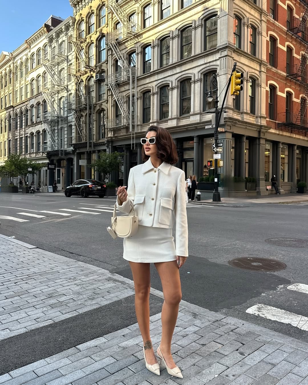 Woman in all-white cropped jacket and mini skirt co-ord with white slingback heels on a SoHo street corner, NYC summer outfit