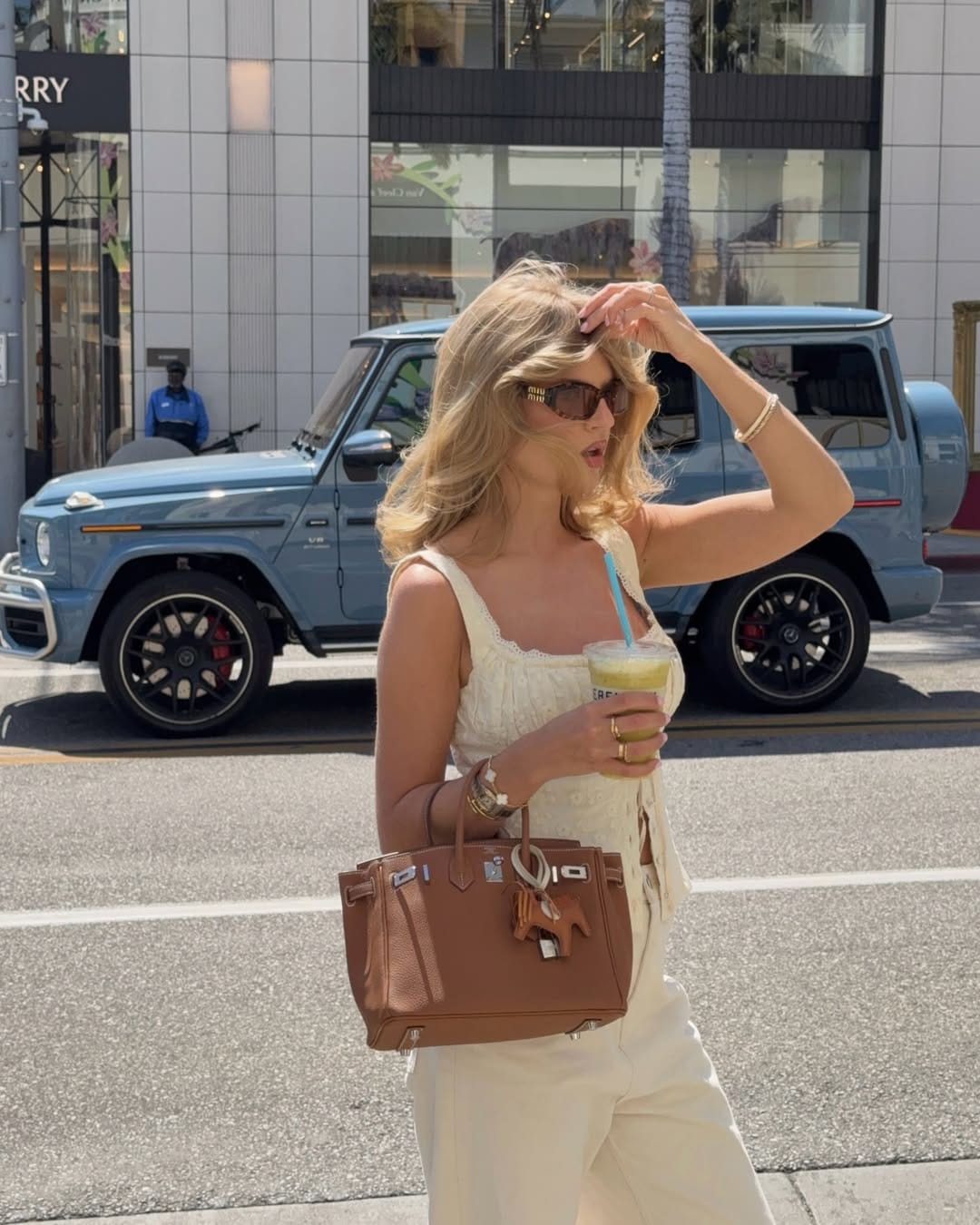  Woman in ivory lace-trim cami and cream wide-leg trousers with tan leather tote and gold bangles, NYC summer aesthetic on a bright street