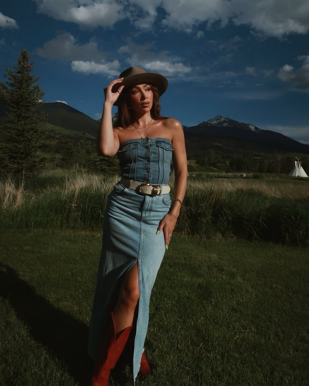 Strapless denim maxi dress with red cowboy boots and olive hat for a country festival look