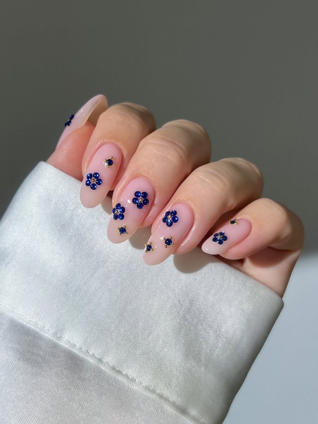 Navy rhinestone flower nails on sheer nude base for a june nail design