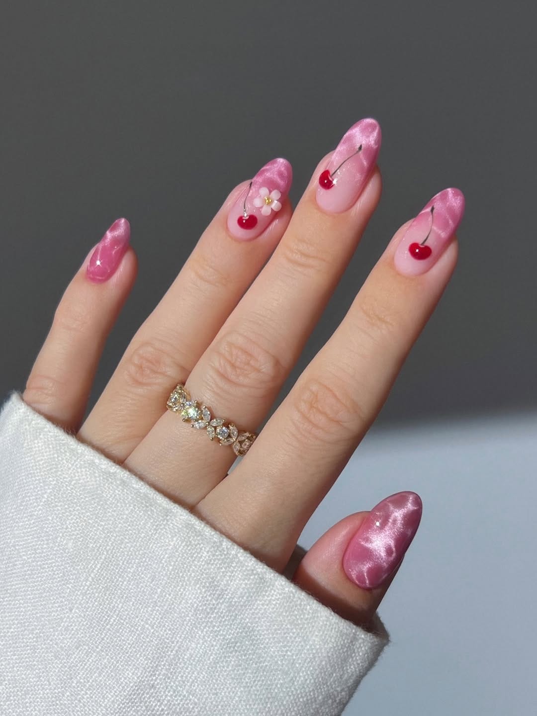 Pink satin cat-eye nails with cherry and daisy detail for a june nail idea
