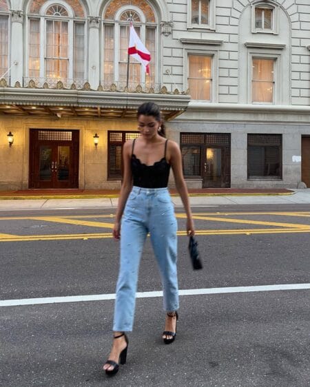 Woman in a black lace cami and light wash high-waisted jeans with strappy black platform heels