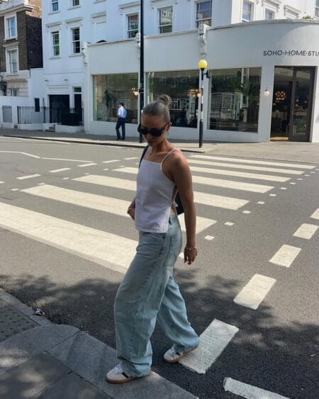 Woman in a white cami and baggy light wash jeans with white trainers crossing a street