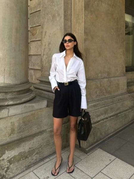 Woman in a crisp white shirt and tailored black Bermuda shorts with a black top-handle bag