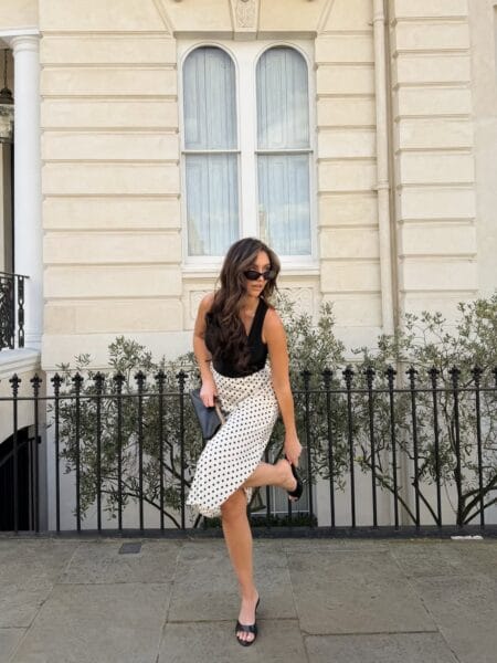 Woman in a black halter top and cream polka dot midi skirt with black mule sandals