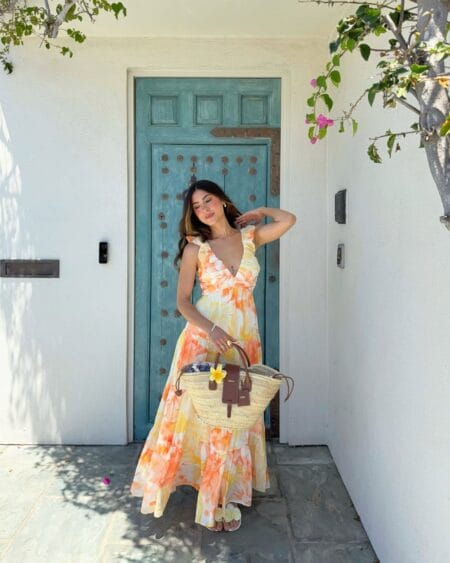 Woman in a watercolour orange and yellow floral maxi dress holding a straw basket bag