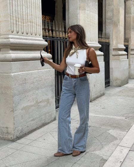 Woman in a white tank and light wash wide-leg jeans with a silk neck scarf and ballet flats