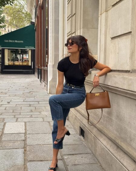 Woman in a black tee and cropped straight jeans with a tan top-handle bag and black heeled mules