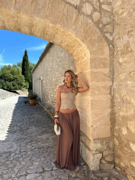 Woman in a cream lace corset top and flowing taupe maxi skirt with a beaded necklace