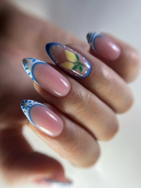 Long almond nails with white French tips painted in blue Portuguese tile patterns and a yellow lemon accent nail