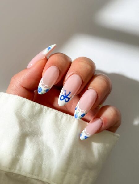 Almond nails with white French tips, hand-painted cobalt blue roses, lace border detail and a bold blue bow accent nail