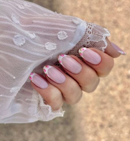 Sheer pink oval nails with white French tips hand-painted with delicate pink rose clusters and sage green leaf detail