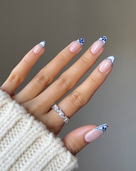 Long almond nails with white French tips decorated in cobalt blue dot-work patterns and petal arrangements on a sheer pink base