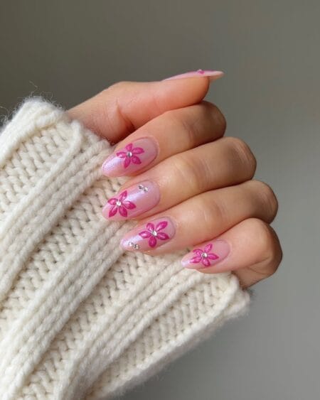 Short oval nails with sheer pink shimmer base and hand-painted hot pink five-petal flowers with silver crystal bead centres