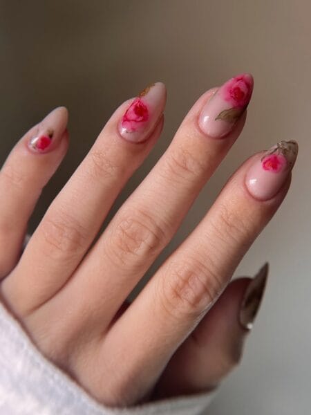 Sheer milky almond nails with hand-painted hot pink roses and dried botanical leaf details at the cuticle