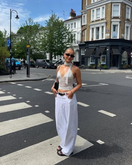 Sheer polka dot mesh halter crop top and white wide-leg jeans with black belt and quilted chain bag — summer casual outfits 2026