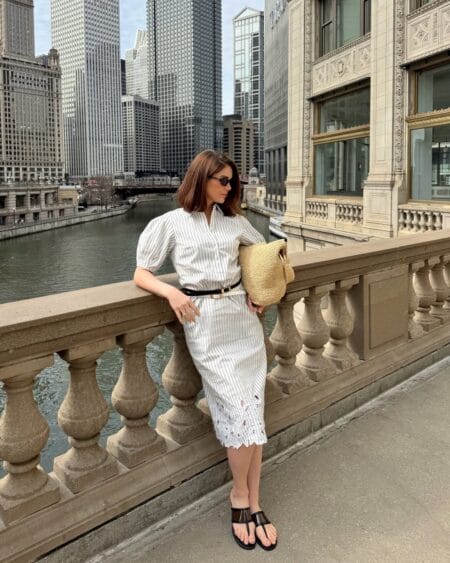 White and grey pinstripe puff-sleeve midi dress with broderie hem belted with black leather belt and raffia tote — june outfit ideas