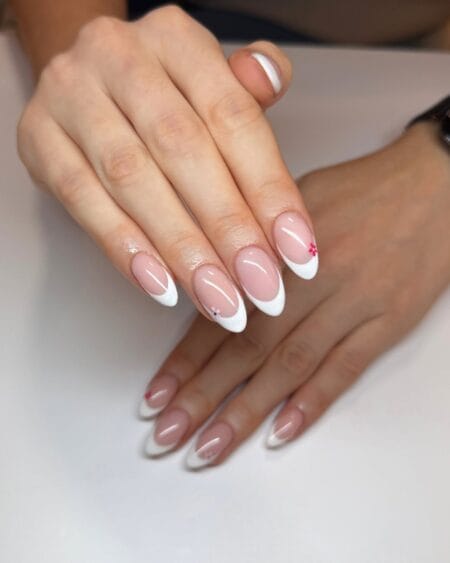 Almond nails with white French tips and delicate micro floral accents on a sheer nude base.