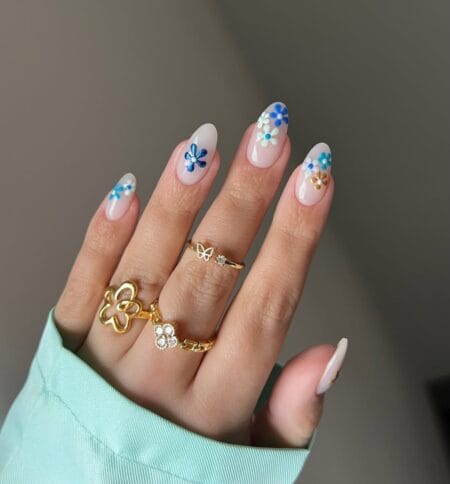 Sheer nude almond nails with clusters of hand-painted blue daisies.