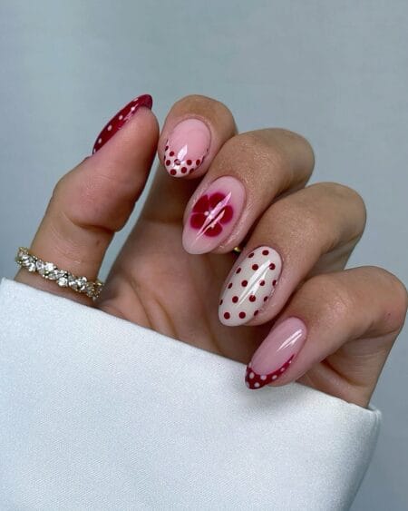 Cherry red almond nails featuring a mix of polka dot and floral nail art.