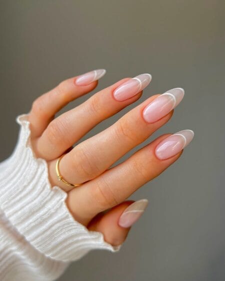 Minimalist almond nails featuring thin white French tips on a nude base.