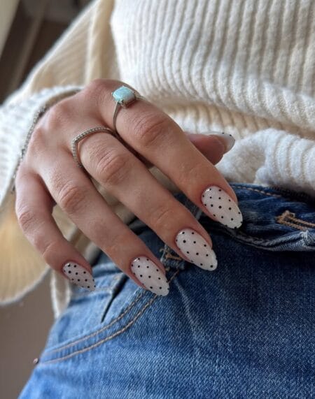 Ivory white almond nails decorated with tiny black polka dots.