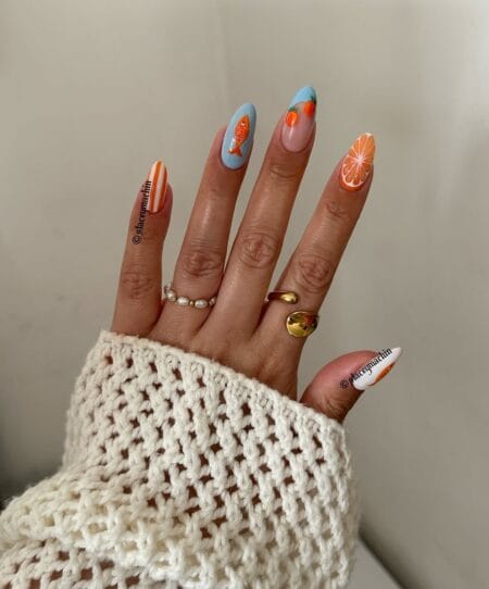 Medium almond nails combining white and marigold orange pinstripe nails with sky blue accent nails carrying golden orange fish — orange fish and citrus coastal nails 2026