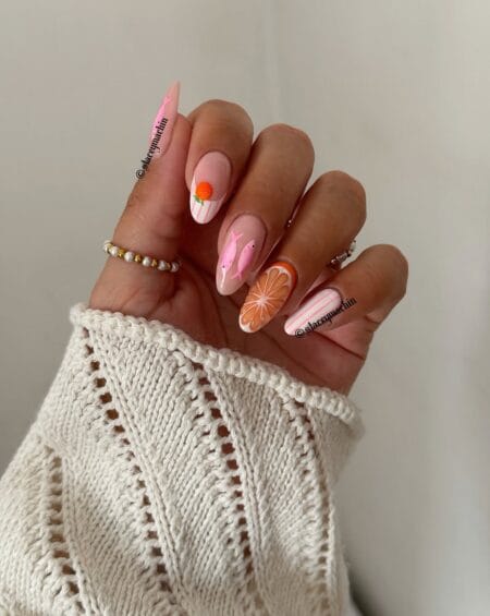 Long blush almond nails with hand-painted pink dolphin silhouettes, 3D orange fruit charm, orange slice nail and pink stripe — pink dolphin and citrus fish nails 2026