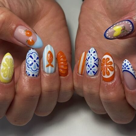 Long almond nails combining Mediterranean blue tile pattern, orange sardine on blue stripe nail, 3D croissant charm and citrus slice designs — Mediterranean tile and sardine nails 2026