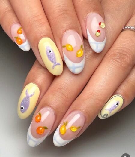 Medium almond nails with glittery lavender sardine on butter yellow base, sheer French nails with tangerine and cherry charms — lavender sardine and citrus fish nails 2026