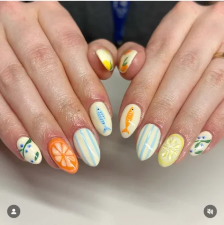 Medium almond nails on warm cream base with blue-grey and orange sardine designs, pinstripe accents and citrus slice nails — sardine and citrus cream stripe nails 2026