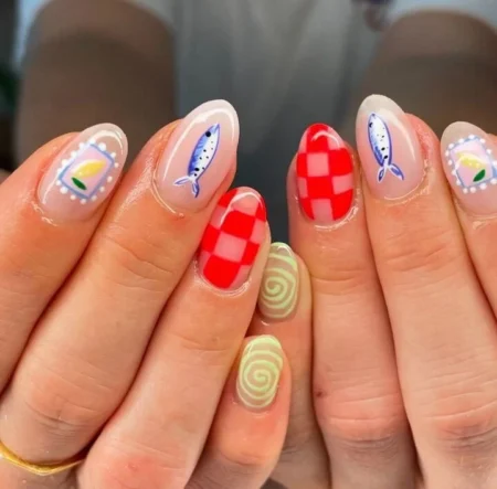 Short round nails combining sheer nude bases with blue sardines, bold red checkerboard nail, sage green spiral nail and lemon stamp cameo — sardine and red check picnic nails 2026