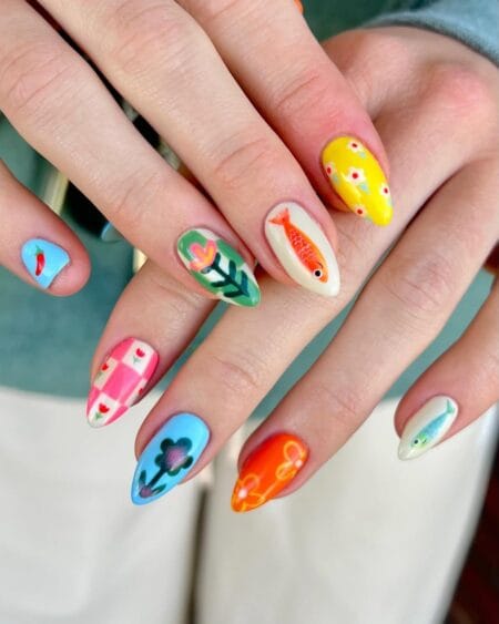 Maximalist almond nails combining folk art orange scaled fish, pink gingham, yellow fish nail and blue floral designs — eclectic fish nail art 2026