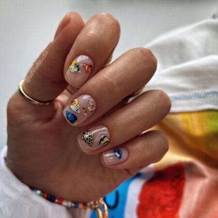 Short square sheer nails with hand-painted tropical reef fish including clownfish, blue tang and angelfish with gold foil flecks — tropical fish nails 2026