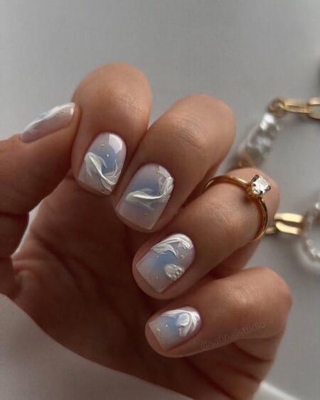 Short square milky blue-white nails with raised 3D sculpted white koi fish curving across each nail with gold foil flecks — white koi fish nails 2026