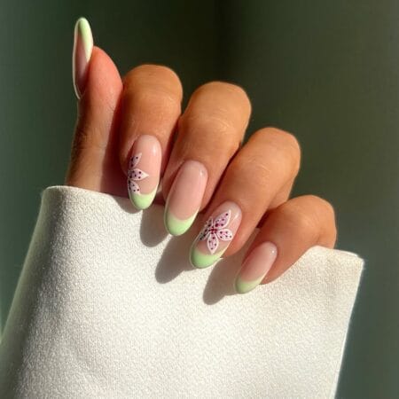 Mint green French tip nails with white flower detail and cranberry dot accents on almond shape
