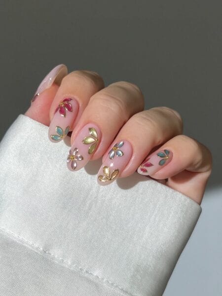 Enamel petal jewel nails with raised metallic flower petals in pink sage gold and blue on sheer nude