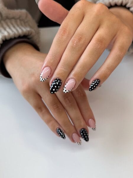 Black and white polka dot almond nails with alternating black and white bases and scattered dot pattern