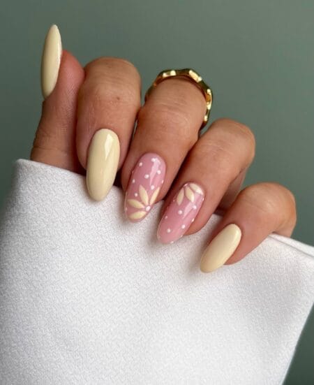 Butter yellow and blush polka dot nails with painted botanical leaf motifs on almond shape