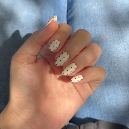 Cream and black minimalist polka dot almond nails with evenly spaced small dots on off-white base