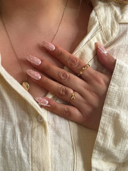 Nude pink polka dot almond nails with loosely scattered white dots on sheer glossy base