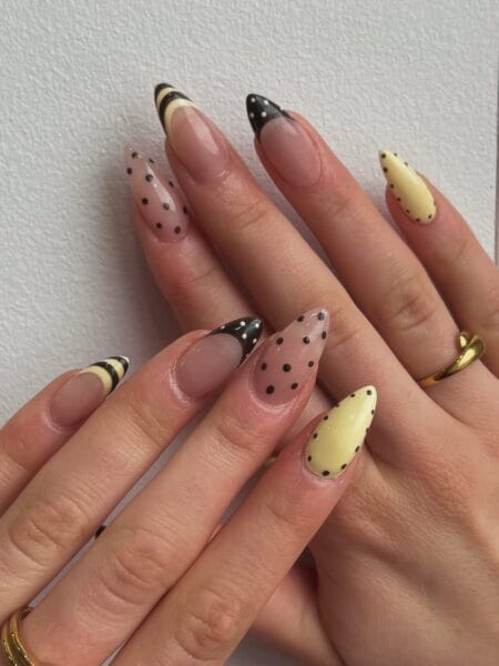 Butter yellow and black retro stripe polka dot nails with horizontal stripe accent on long pointed almond nails