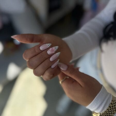 Black dot French tip almond nails with 3D pink flower accent on sheer nude base