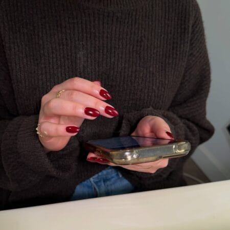 Glossy maroon almond nails worn with a chunky knit