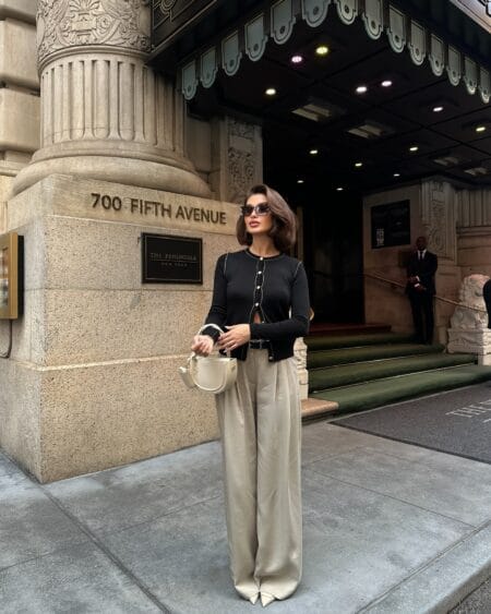 Woman in a black contrast-stitch cardigan with champagne satin wide-leg trousers and an ivory bag